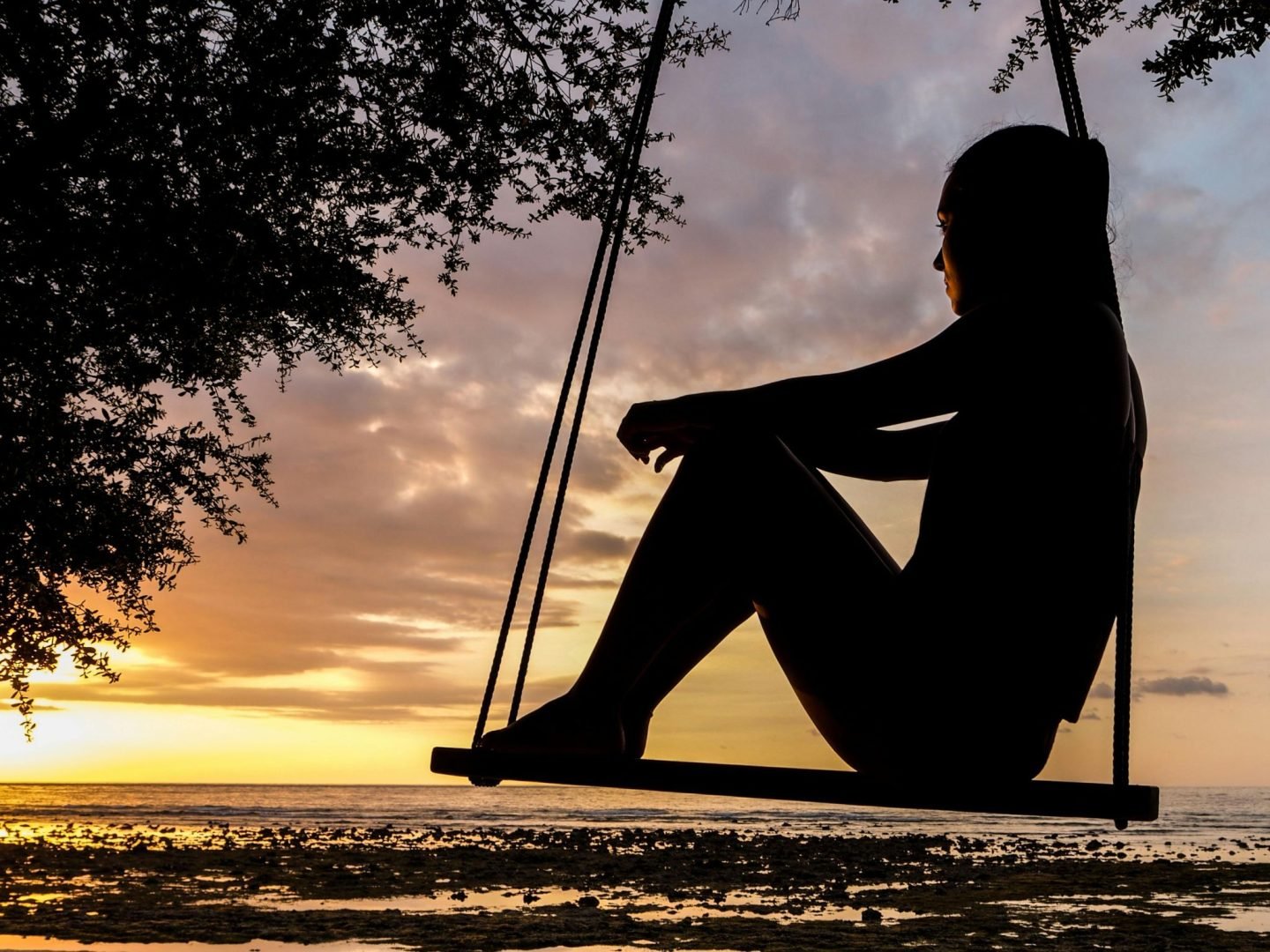 women sitting on chair swing that is silhouetted in the sunset