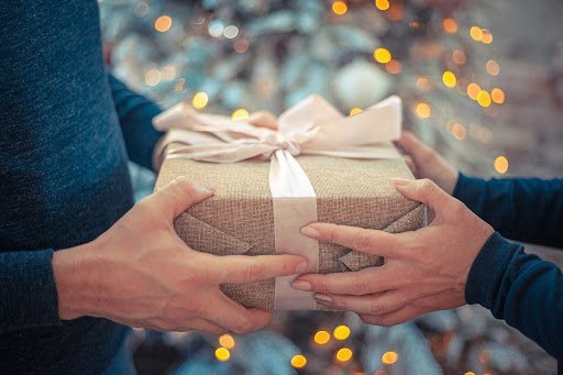 two people holding a celebration box together with a bokeh Christmas tree in the background