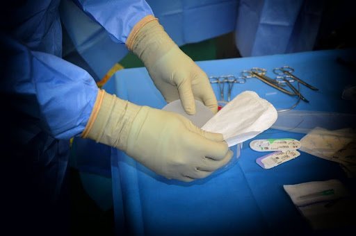 man in plastic surgery with yellow gloves on against blue 