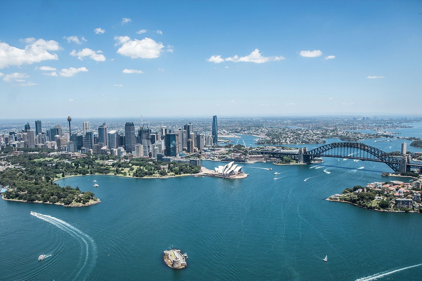 Aerial view of Sydney Harbour featuring the Opera House, Harbour Bridge, city skyline and surrounding blue waters on a sunny day